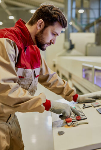 Production line worker operating automated machine for wood processing at industrial facility.